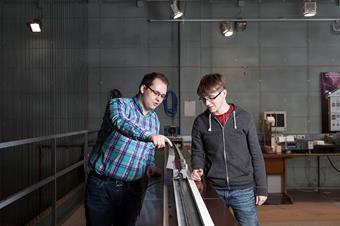 The picture shows two male students in a laboratory of electrical machines.
